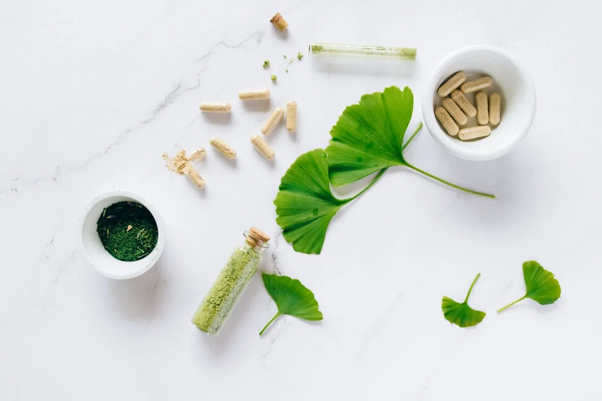 Pflanzliche Kapseln, Kräuterpulver und Ginkgoblätter auf einem hellen Tisch